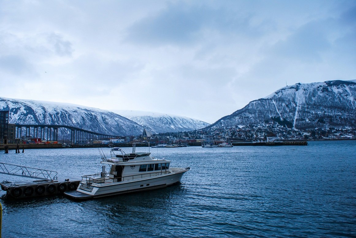 Boat moored in Tromsø harbour with the Arctic Cathedral, Tromsø Bridge and snow-covered mountains in winter